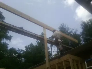 Carpenter setting a ridge beam over a new addition frame in Liberty